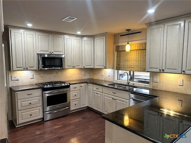 kitchen with dark wood-type flooring, sink, hanging light fixtures, dark stone countertops, and stainless steel appliances