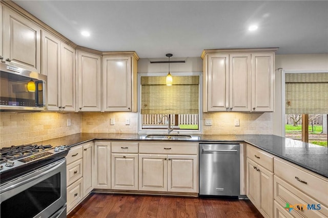 kitchen with pendant lighting, sink, dark stone countertops, stainless steel appliances, and dark hardwood / wood-style floors