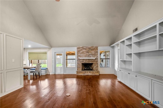 unfurnished living room featuring dark wood-type flooring, high vaulted ceiling, and a large fireplace