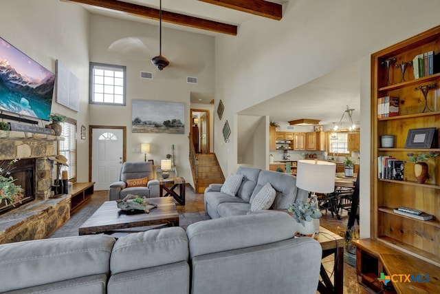 living room with a stone fireplace, beam ceiling, hardwood / wood-style flooring, a high ceiling, and ceiling fan with notable chandelier