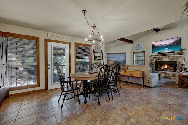 dining space with a stone fireplace, lofted ceiling, and an inviting chandelier