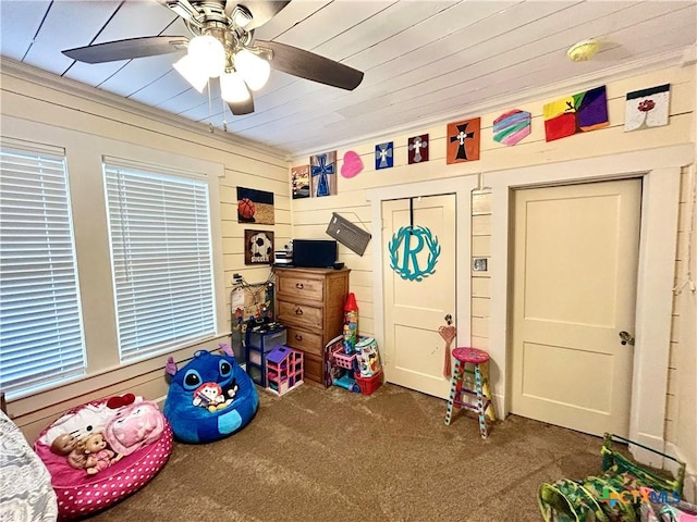 playroom with ceiling fan, dark carpet, and wood walls