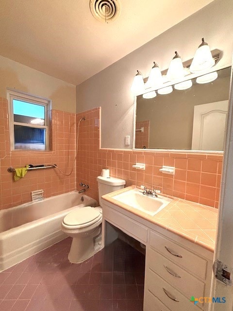 full bathroom with tile patterned floors, sink, tiled shower / bath, toilet, and tile walls