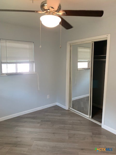 unfurnished bedroom with multiple windows, ceiling fan, a closet, and hardwood / wood-style flooring