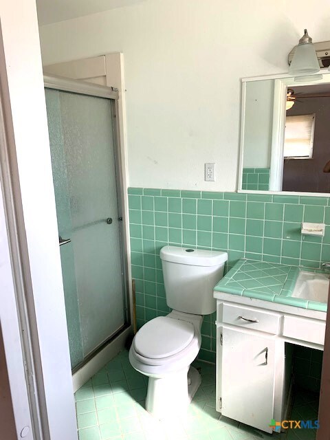 bathroom featuring walk in shower, tile patterned floors, toilet, vanity, and tile walls