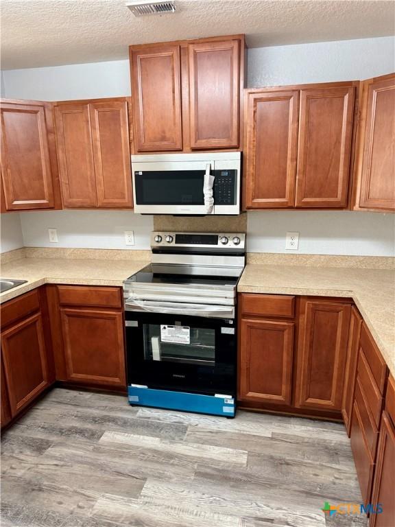 1037 N Guadalupe St, Seguin, TX 78155 - kitchen with stainless steel electric range, light countertops, light wood-style floors, a textured ceiling, and brown cabinetry