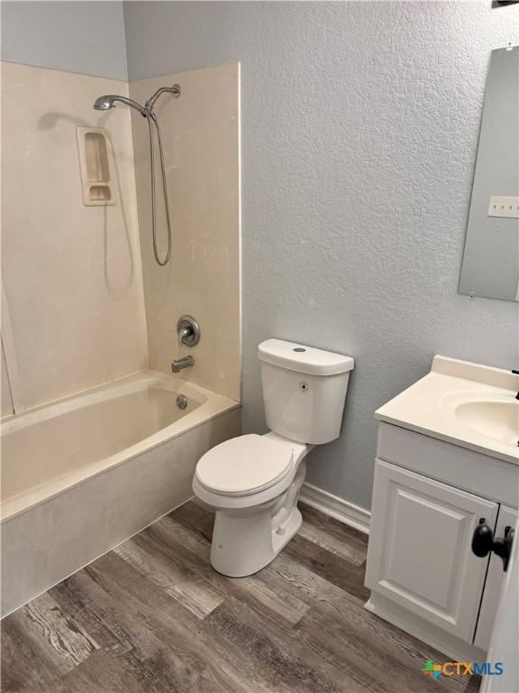 1037 N Guadalupe St, Seguin, TX 78155 - full bath featuring wood finished floors, a textured wall, vanity, bathing tub / shower combination, and toilet