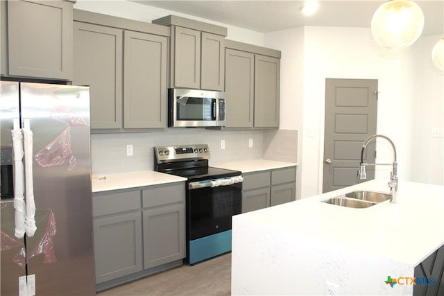 kitchen with sink, gray cabinets, appliances with stainless steel finishes, tasteful backsplash, and light hardwood / wood-style floors