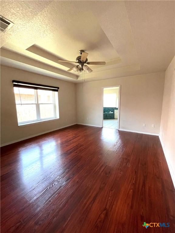 unfurnished room featuring a raised ceiling, dark wood-type flooring, baseboards, a ceiling fan, and a textured ceiling
