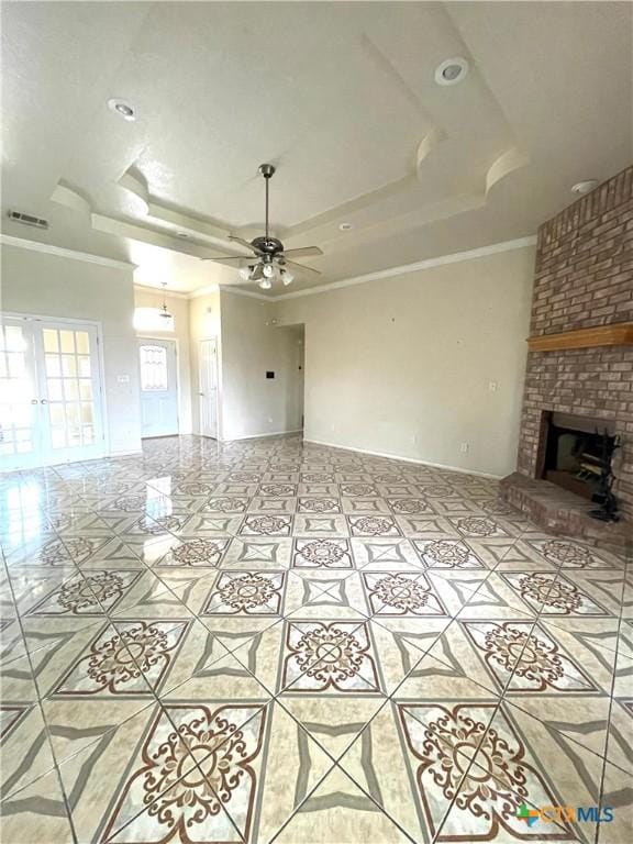 unfurnished living room featuring ornamental molding, a tray ceiling, ceiling fan, light tile patterned floors, and a brick fireplace