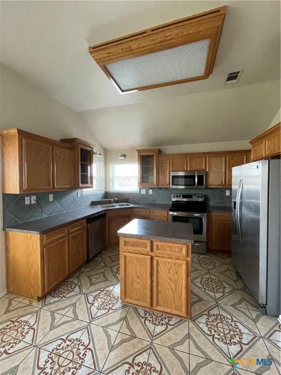 kitchen featuring appliances with stainless steel finishes, a sink, decorative backsplash, vaulted ceiling, and dark countertops