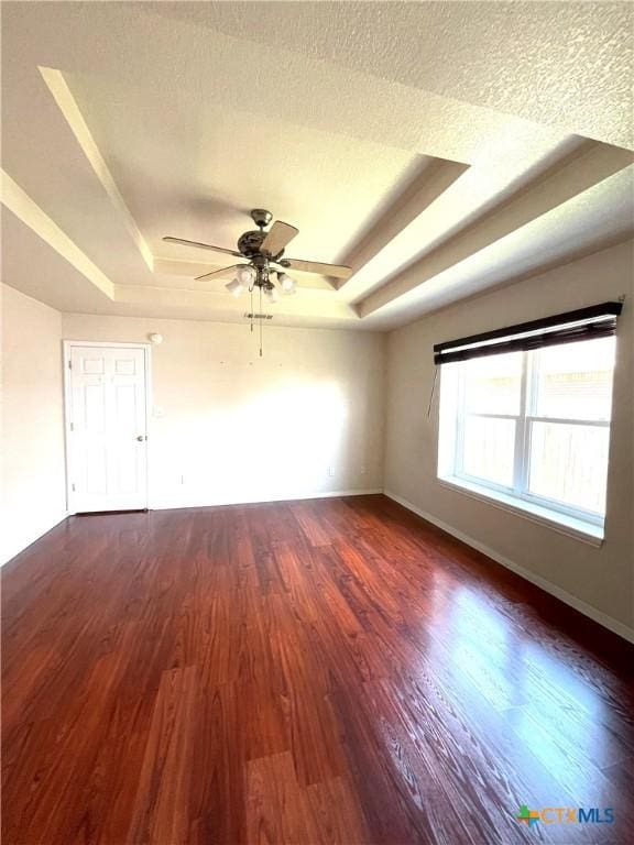 empty room with a tray ceiling, dark wood-type flooring, ceiling fan, and baseboards