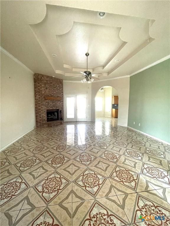 unfurnished living room with a raised ceiling, a ceiling fan, tile patterned floors, arched walkways, and a fireplace