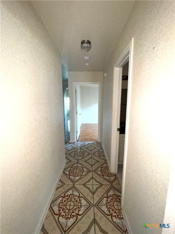 hallway featuring light tile patterned floors, baseboards, and a textured wall