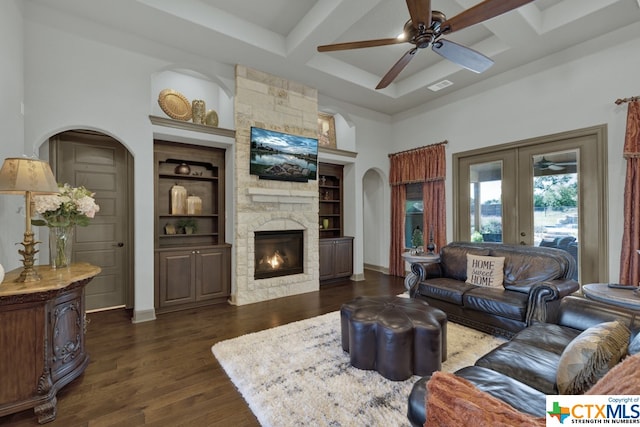 living room featuring dark hardwood / wood-style floors, beam ceiling, ceiling fan, a fireplace, and built in features