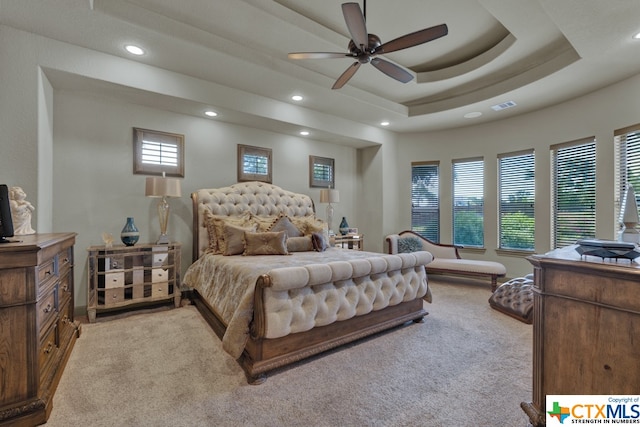 bedroom featuring ceiling fan, a raised ceiling, and light colored carpet