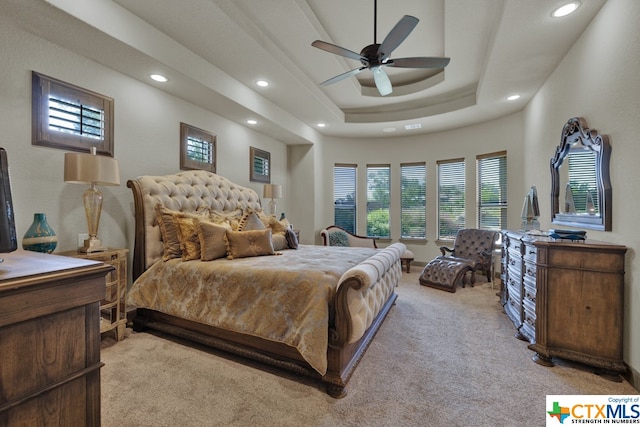 bedroom with light carpet, ceiling fan, and a tray ceiling