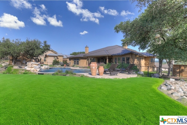 rear view of property featuring a patio, a lawn, and a pool