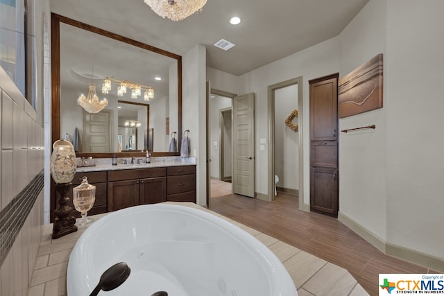 bathroom featuring toilet, vanity, an inviting chandelier, and a bathtub