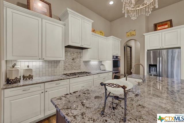 kitchen featuring white cabinetry, light stone counters, appliances with stainless steel finishes, an inviting chandelier, and pendant lighting