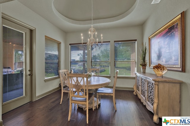 dining area featuring dark wood-type flooring, a chandelier, and a raised ceiling