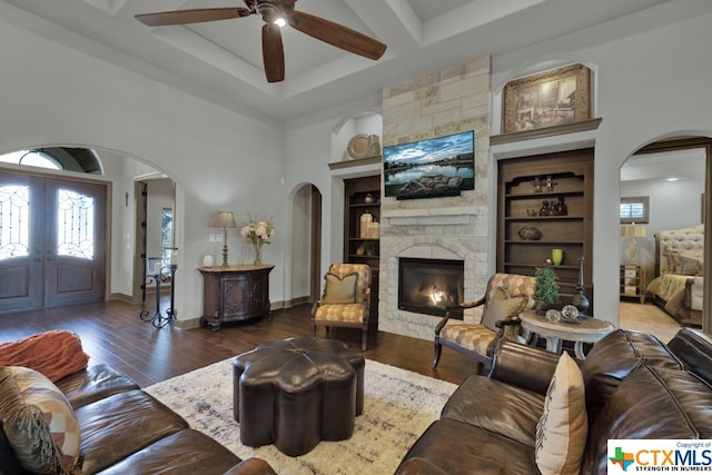 living room featuring built in shelves, dark hardwood / wood-style flooring, ceiling fan, and a stone fireplace