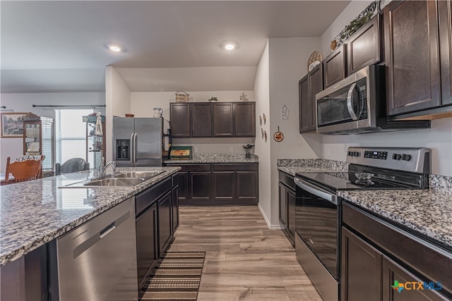 kitchen featuring stainless steel appliances, dark brown cabinets, light wood-type flooring, and light stone counters