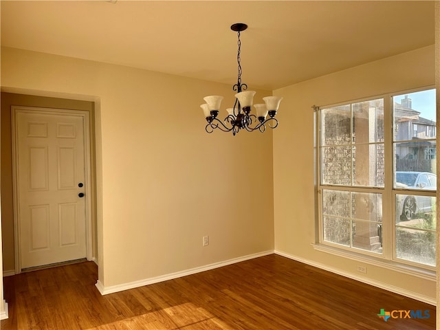 spare room with an inviting chandelier, a wealth of natural light, and hardwood / wood-style floors