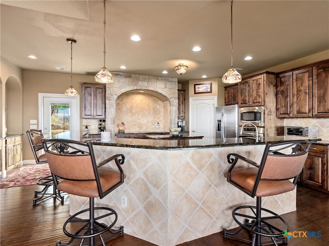 kitchen with stainless steel appliances, backsplash, pendant lighting, a breakfast bar, and a center island with sink