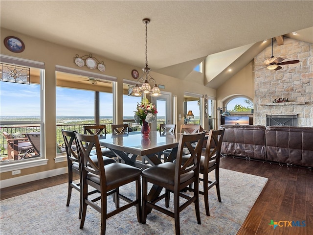 dining space with ceiling fan with notable chandelier, vaulted ceiling, a textured ceiling, a fireplace, and dark hardwood / wood-style flooring