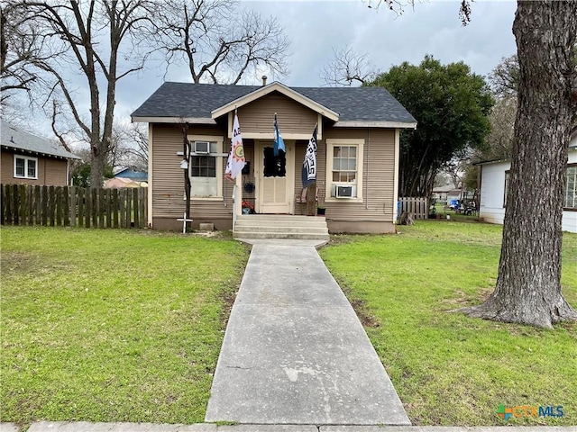 bungalow-style home with cooling unit, roof with shingles, fence, and a front lawn