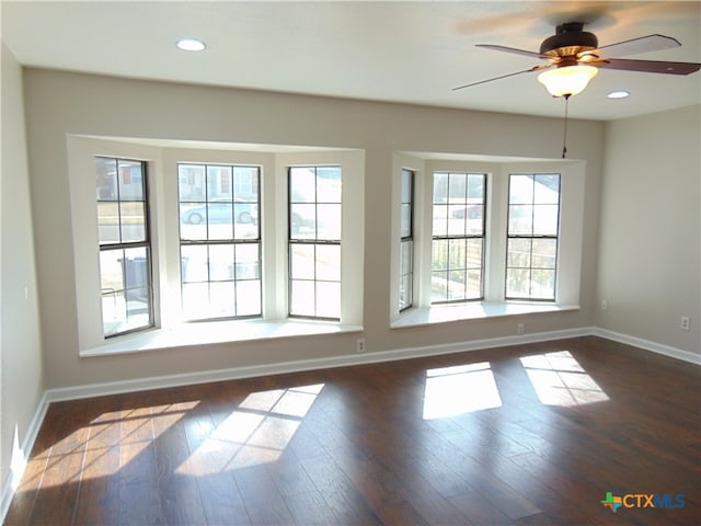 empty room with plenty of natural light, ceiling fan, and dark wood-type flooring