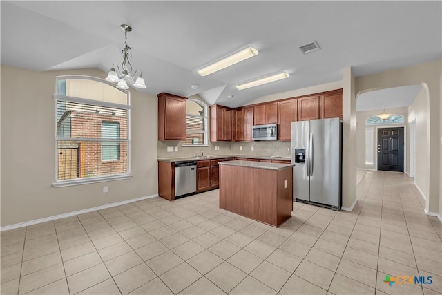 kitchen with stainless steel appliances, visible vents, vaulted ceiling, backsplash, and a center island