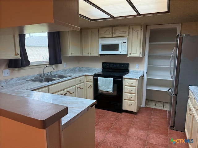 kitchen featuring a sink, black range with electric cooktop, freestanding refrigerator, a peninsula, and white microwave