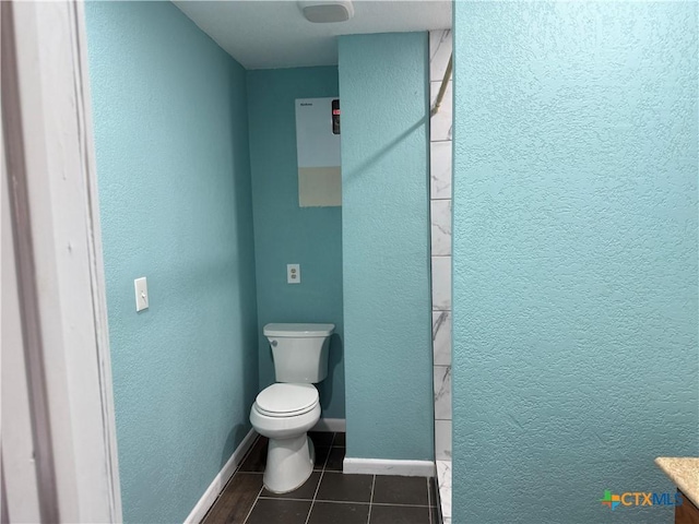 bathroom featuring tile patterned flooring, a textured wall, toilet, and baseboards