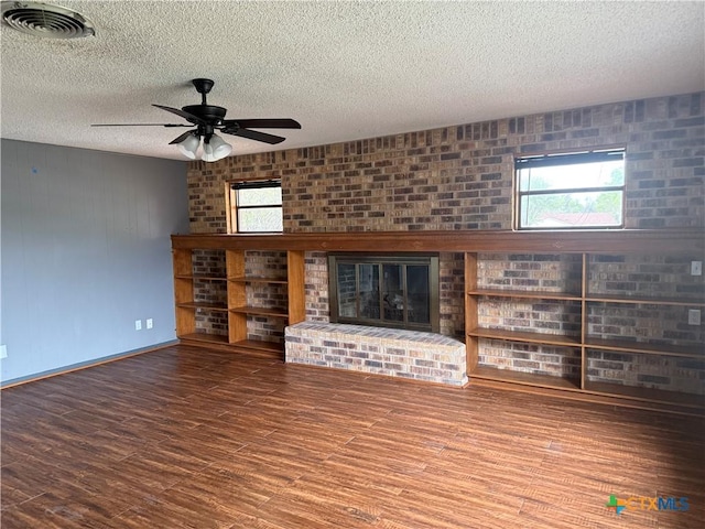 unfurnished living room with visible vents, wood finished floors, ceiling fan, and a brick fireplace