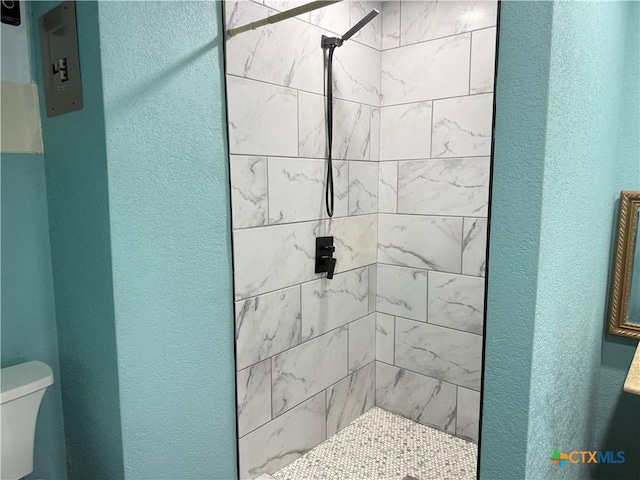 bathroom with a stall shower, toilet, and a textured wall