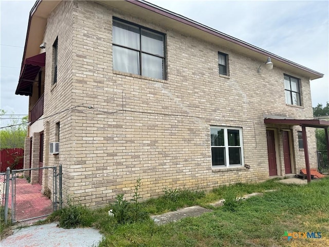 view of side of property featuring cooling unit, a gate, fence, and brick siding