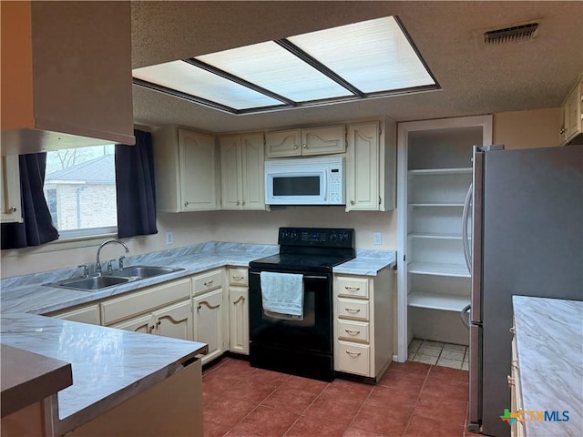 kitchen featuring visible vents, black range with electric cooktop, a sink, white microwave, and freestanding refrigerator