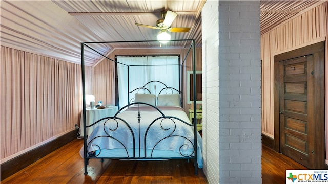 bedroom featuring dark hardwood / wood-style floors, wooden walls, brick wall, and vaulted ceiling