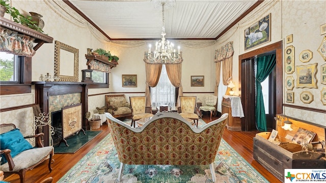 living area with a fireplace, a notable chandelier, hardwood / wood-style flooring, and crown molding