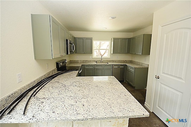 kitchen with gray cabinetry, sink, light stone countertops, and appliances with stainless steel finishes