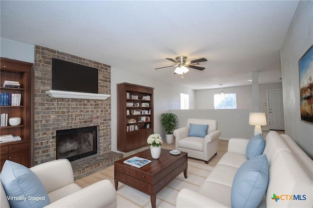 living room featuring a brick fireplace, ceiling fan, and light wood-type flooring