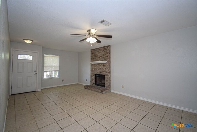 unfurnished living room featuring ceiling fan, a brick fireplace, a textured ceiling, and light tile patterned floors