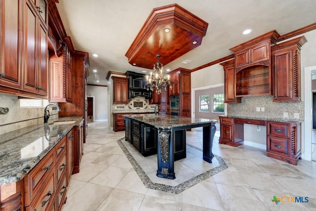 kitchen featuring crown molding, sink, a center island with sink, and dark stone counters