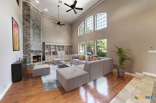 living room featuring ceiling fan, a high ceiling, wood-type flooring, ornamental molding, and a stone fireplace