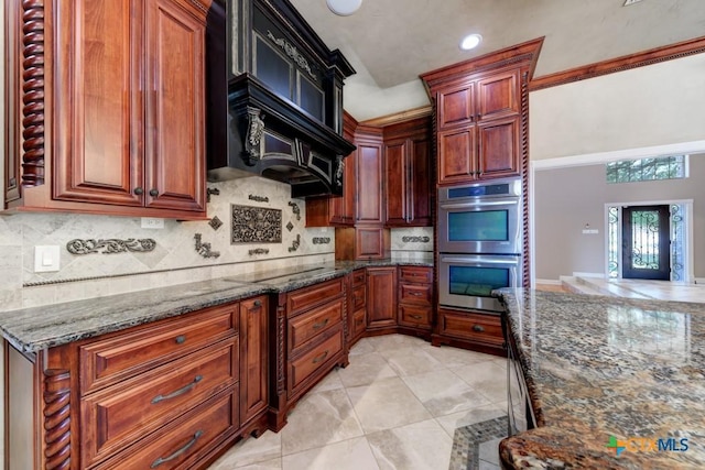 kitchen with custom exhaust hood, black electric cooktop, double oven, and dark stone counters