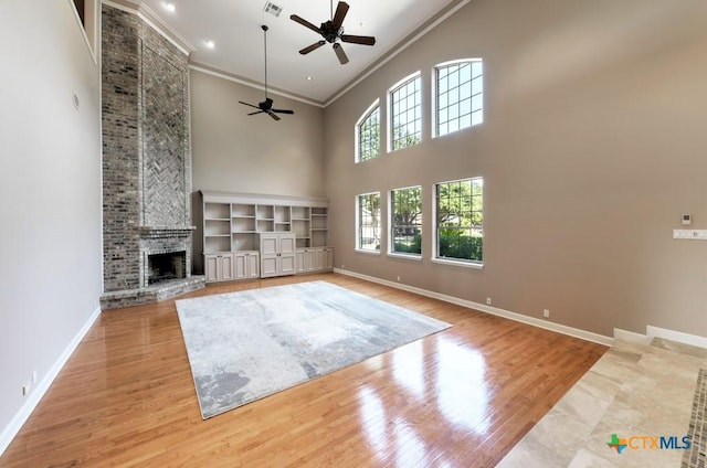 unfurnished living room with crown molding, light wood-type flooring, ceiling fan, a fireplace, and a high ceiling