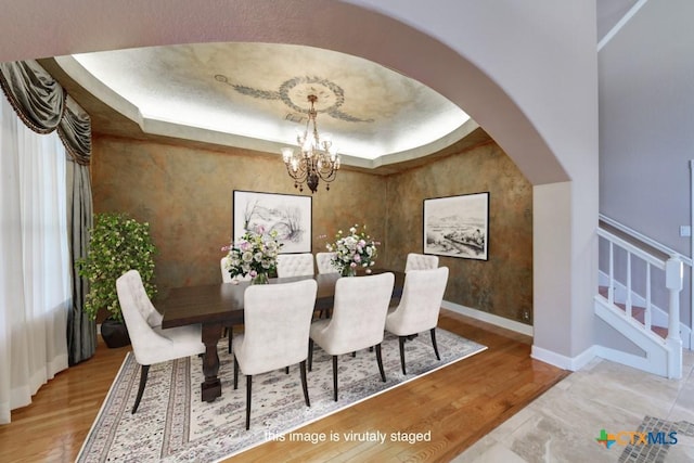 dining area with a tray ceiling, a chandelier, and hardwood / wood-style flooring