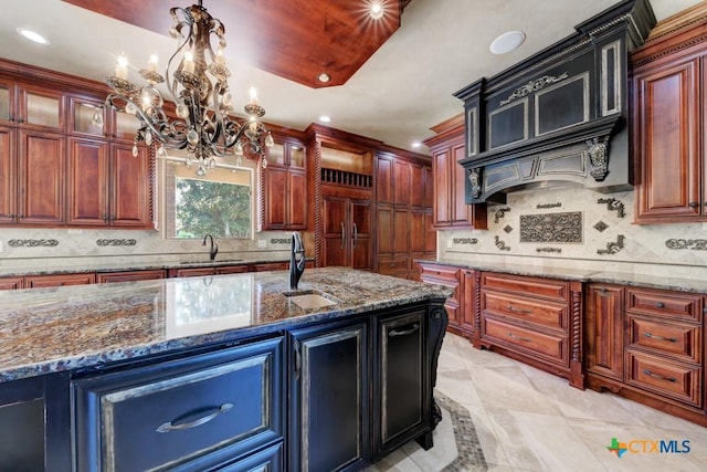 kitchen featuring hanging light fixtures, an island with sink, tasteful backsplash, and stone countertops